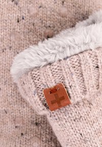 Helles rosa gestricktes Accessoire mit flauschigem weißen Besatz. Verfügt über ein kleines braunes Etikett mit einem Kreuzemblem und zeigt ein strukturiertes Strickmuster.