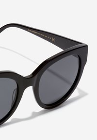 Mustat aurinkolasit, joissa on paksu, kulmikas kehys. Linssit ovat tummanharmaat, ja temppeleissä on kohokuvioidut yksityiskohdat. Siisti, kiiltävä pinta.