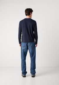 Long-sleeve navy T-shirt paired with loose-fit blue jeans. The jeans have a classic five-pocket design with visible stitching on the back.