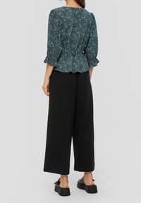 Blusa a stampa floreale in turchese e nero con maniche a tre quarti e orlo arricciato, abbinata a pantaloni larghi neri a gamba larga e sandali con plateau.