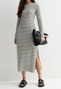 Robe à manches longues rayée en noir et blanc, avec une fente sur le côté. Portée avec des sandales noires et un sac noir texturé.
