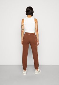 Ruskeat collegehousut, joissa on sivutaskut, elastiset hihnat ja kontrastivärinen keltainen ompelu, yhdistettynä tiukkaan valkoiseen toppiin.