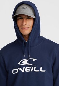 Navy blue hoodie with a front kangaroo pocket and white O'Neill logo, paired with a gray cap featuring a matching logo. Cotton blend fabric.