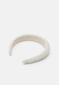 Fehér szövet fejpánt, amely texturált mintával rendelkezik, és egyenletesen elhelyezett kis gyöngyök díszítik a külső felületét. Sima belső bélés.