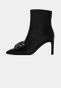 Bottine noire à bout pointu, talon stiletto haut et nœud décoratif sur le devant.