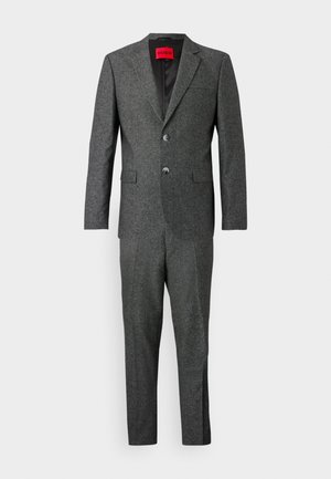 Traje gris texturizado con dos botones, solapas de muesca y bolsillos laterales. Etiqueta de marca visible en el interior del cuello. Corte entallado y líneas limpias.
