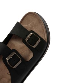 Sandal in pelle nera con due cinturini regolabili, fibbie in argento e una soletta in suede color beige. Punta arrotondata e dettagli testurizzati sulla suola.