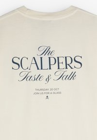Camiseta color crema con texto navy en la parte posterior: "The SCALPERS Taste & Talk," con detalles del evento y un logo de calavera.