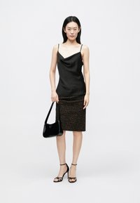 Musta satiininen liivimekko, jossa laskeutuva etuosio, yhdistetty ruskeaan leopardikuvioiseen kynähameeseen. Malli kantaa kiiltävää mustaa käsilaukkua ja käyttää hihnallisia korkokenkiä.