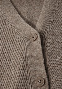 Beige pletený kardigan s výstřihem do V, žebrovanou texturou a dvěma hnědými knoflíky vpředu. Hladká tkanina s jemnými barevnými variacemi.