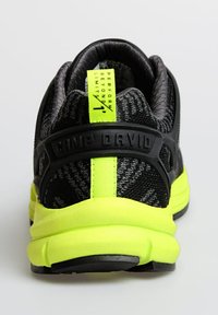 Black athletic shoe with a textured knit upper, reflective accents, and a bright yellow sole. Features a prominent heel tag and logo.