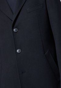 Blazer in misto lana blu navy con design sartoriale, due bottoni, una tasca sul petto e dettagli di cucitura sottili sulla revers e sulle tasche.