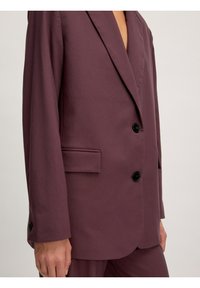 Bordeauxfarbener Blazer mit glatter Textur, breiten Revers, zwei schwarzen Knöpfen und einer einzigen Brusttasche. Taillierte Passform, seitlich präsentiert.