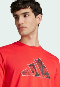 T-shirt di cotone rossa con un grande logo grafico nero e rosso caratterizzato da un motivo testurizzato. Design con maniche corte e collo a giro.