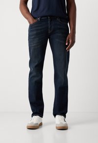 Jeans negri închis, cu croi drept, cu o ușoară decolorare, cinci buzunare și un brâu solid cu bucle pentru curea. Purtați cu adidași albi.