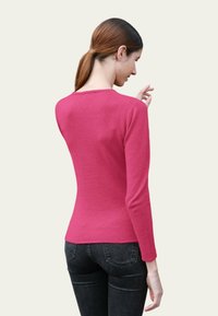 Haut à manches longues ajusté en tricot rose vif avec un col rond, texture lisse et détails cousus aux épaules.