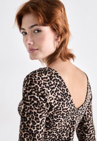 Langermet topp med leopardmønster i elastisk stoff med dyp V-utringning bak. Har en tettsittende silhuett og subtil ribbestruktur.