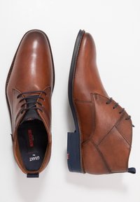 Bottines en cuir marron avec une finition lisse, un design à lacets et des accents texturés. Talon renforcé et semelle en caoutchouc bleue.