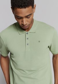 Lichtgroene polo in katoen, met een kraag, een drukknoopsluiting met drie knopen en een subtiel logo op de linkerborst.