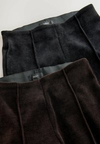 Zwei Paare aus Cord-Hosen in dunklen Farben, eine schwarz und eine dunkelbraun, mit einer gerippten Struktur und einem einfachen Bund mit Markenlabel.