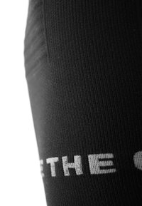 Schwarze Sportleggings mit strukturiertem Rippmaterial und weißen Kontrastlogo. Nahaufnahme hebt die Material- und Formdetails hervor.