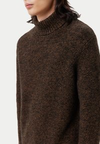 Brauner Strickrollkragenpullover mit einem strukturierten Muster, einem gerippten Kragen und einer glatten Oberfläche, die verschiedene Brauntöne zeigt.