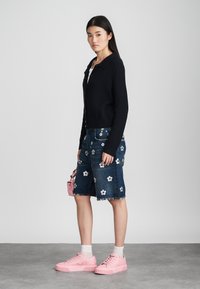 Cardigan de malha escura, calções de denim tipo bermuda com bordado floral, ténis plataforma cor-de-rosa e uma pequena mala cor-de-rosa.