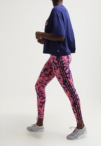 Námořnické oversized tričko v kombinaci s legínami s živým růžovým květinovým vzorem, které mají černé boční proužky. Model má na sobě šedé tenisky.