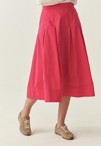 Fuksiahõlmikseeliku, millel on sile tekstuur, põlvpikkus, lai vöökoht ja sirge äär, koos beežide tossudega.