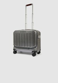 Zilverkleurige harde koffer met verticale ribbels, uittrekbare handgreep en vier zwarte wielen. Heeft een combinatieslot aan de zijkant.