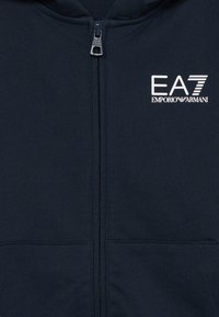 Felpa con zip blu navy in un materiale morbido, con zip argentata e logo EA7 Emporio Armani sul petto. Due tasche frontali.