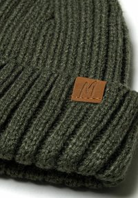 Olive green knitted beanie with ribbed texture and a folded cuff. Features a brown rectangular leather patch labeled "M."
