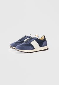 Sapatilhas de desporto em azul-marinho e azul claro, com materiais em camurça e couro, apresentando uma faixa branca, calcanhar preto e sola de borracha texturizada.