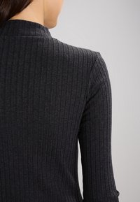 Mörkgrå ribbad tröja med hög halsringning och långa ärmar, med vertikala ränder och en jämn textur.