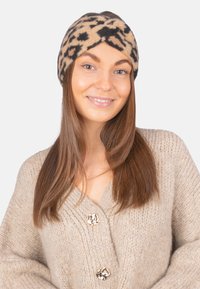 Bandeau beige imprimé léopard en tissu doux. Présente un design torsadé à l'avant et une texture lisse. Convient pour une tenue décontractée.