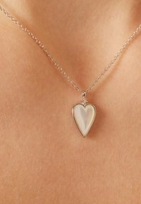 Zilveren ketting met een hartvormige hanger met een glanzend, iriserend oppervlak en een klein decoratief accent aan de bovenkant.