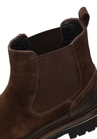 Bruine suède enkellaars met elastische zijpanelen, textuur ribbeling en een stevige zool. Gladde afwerking met contrasterende stiksels en een lus.