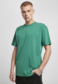 Tricou verde din bumbac, cu guler rotund, mâneci scurte și o croială lejeră. Textură netedă, detalii de cusătură minime.