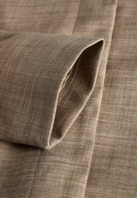 Tuvplāns ar salocītu bēšas krāsas audumu, redzamas šuves un smalka austā tekstūra uz gludas virsmas.