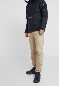 Czarny nylonowy polar z zamkiem błyskawicznym, beżowe spodnie cargo i czarne buty trekkingowe. Minimalistyczny design, praktyczny do użytku na świeżym powietrzu.