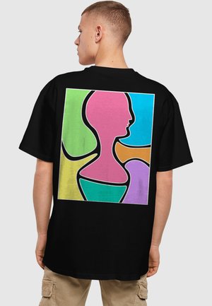 Sort t-shirt med et farverigt abstrakt design på ryggen, med former i pink, grøn, blå, orange og lilla konturer.