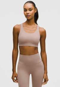 Hellbrauner Sport-BH mit einer glatten, dehnbaren Textur; verfügt über breite Träger und ein schlichtes Design. Getragen mit passenden hoch taillierten Leggings.