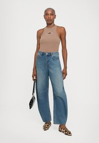 Brun ärmlös bodysuit med en diamantformad utskärning, parat med vida blå jeans. Accentuerad med leopardmönstrade slip-ons och en svart handväska.