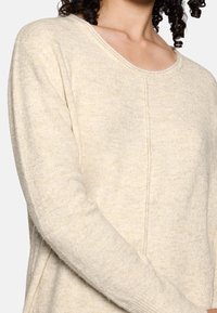 Lichtbeige gebreide trui met een brede halslijn en lange mouwen, met een zachte textuur en subtiele stiksels langs de voorkant.
