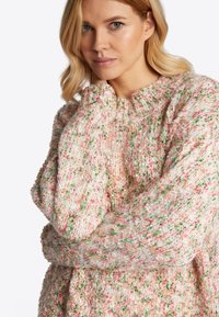 Strickpullover mit einem strukturierten, mehrfarbigen Muster in Rosa, Weiß und Grün. Besitzt einen hohen Kragen und Oversized-Ärmel.