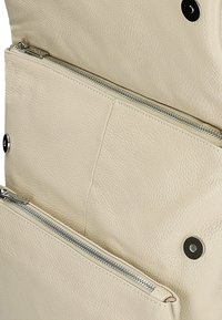 Interno di una borsa in pelle beige chiaro con due tasche con zip e una chiusura a scatto magnetico. La superficie testurizzata aggiunge un dettaglio tattile.