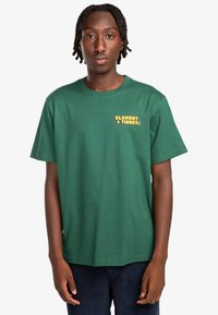 Green cotton t-shirt with short sleeves, featuring "ELEMENT & TIMBER!" printed in yellow on the left chest area. Standard fit.