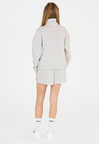 Hellgrauer Pullover mit hohem Kragen, lockerer Passform und gerippten Bündchen, kombiniert mit passenden Shorts. Weiße Sneakers und Socken mit Schriftzug.