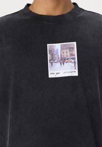 Sort bomulds sweatshirt med et lille trykt billede af en gade i New York med teksten "New York City of Dreams" i hvid skrift.