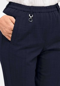 Navyblauwe broek van textuurstof, met een elastische tailleband en een zichtbaar metalen lus aan de voorkant. Twee zijzakken zijn inbegrepen.